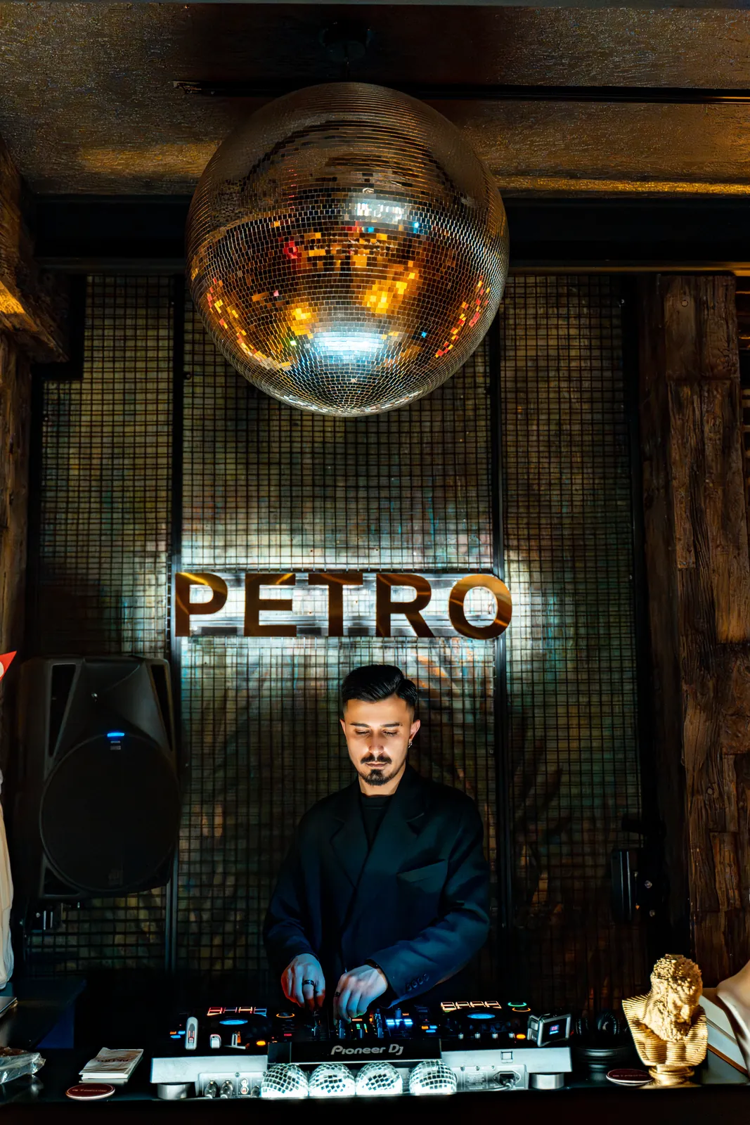 Petro Cocktail Bar — A DJ playing under the mirror ball in front of the PETRO sign
