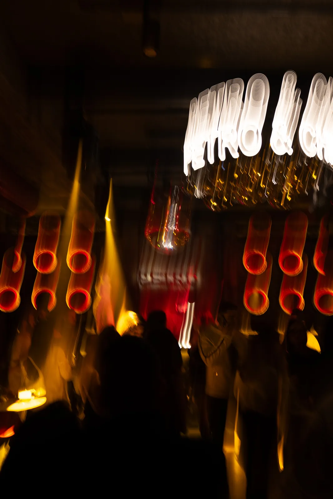 Petro Cocktail Bar — The PETRO & CHILL neon chandelier over a dancing crowd in yellow light beams, seen from a distance