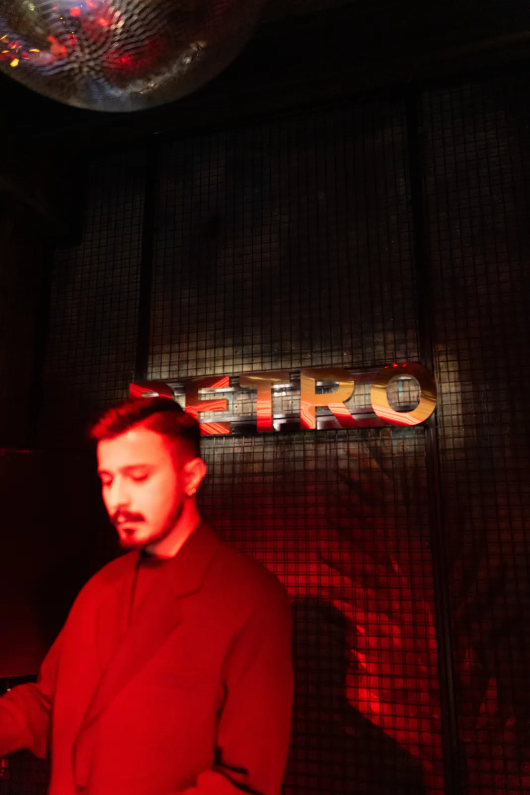 Petro Cocktail Bar — A DJ in red light with the PETRO letters behind him