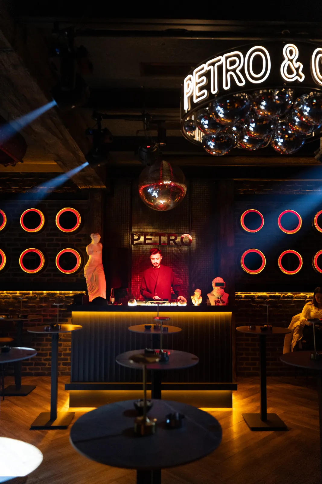 Petro Cocktail Bar — Wide view of the venue: the neon chandelier, statues, red neon rings and the DJ booth